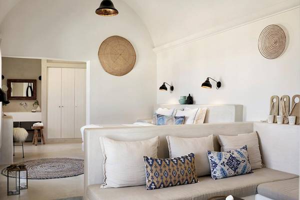 Schlafzimmer im Santo Pure Oia Suites & Villas Hotel mit weißen Wänden und Möbeln, Kissen und Lampen.