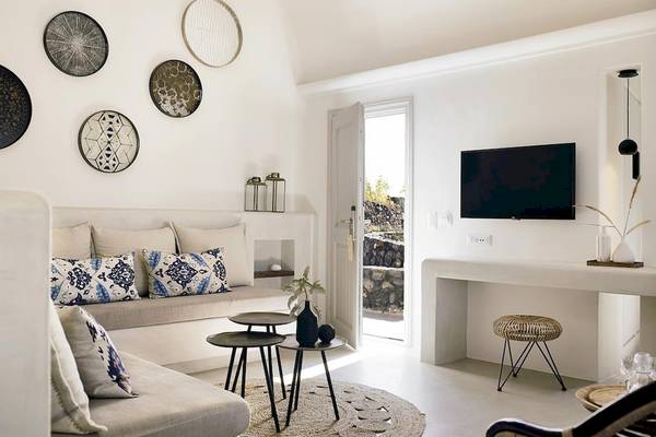 Wohnbereich des Santo Pure Oia Suites & Villas Hotels mit Sofa, Tisch, Fernseher und offenen Türen.