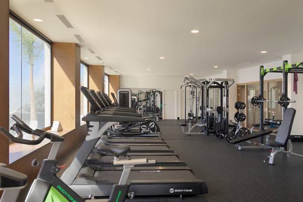 Fitnessstudio im H10 Atlantic Sunset Hotel mit Geräten und Blick auf Palmen.