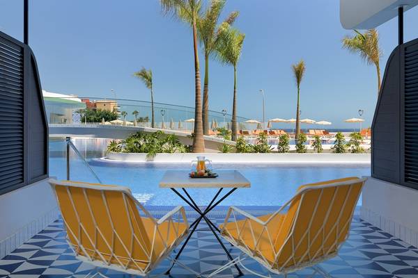 Blick auf den Poolbereich des H10 Atlantic Sunset Hotels mit zwei gelben Stühlen und einem Tisch.