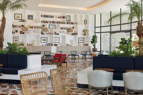 Innenansicht der Lobby des H10 Atlantic Sunset Hotels mit weißen Wänden, Bücherregalen, Pflanzen und verschiedenen Sitzgelegenheiten.
