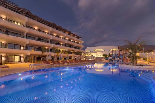 Nachtansicht des Swimmingpools des H10 Atlantic Sunset Hotels mit leuchtenden blauen Wasser und umliegenden Sonnenliegen.