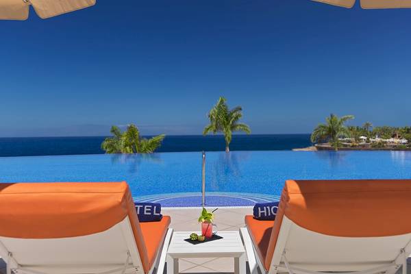 Zwei orangefarbene Liegestühle am Pool des H10 Atlantic Sunset Hotels mit Blick auf das Meer.