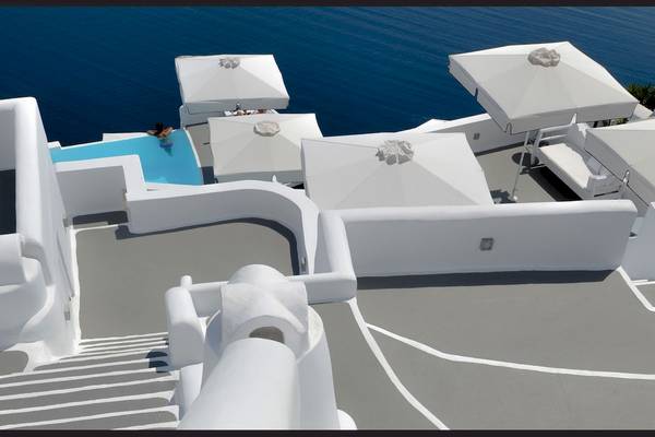 Oberirdisches Hotel mit Pool und Meerblick auf Santorini, weiß gekleidete Terrasse.