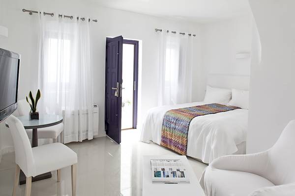 Innenansicht eines Zimmers im Katikies Chromata Santorini Hotel mit weißem Bett, Tisch und Fernseher
