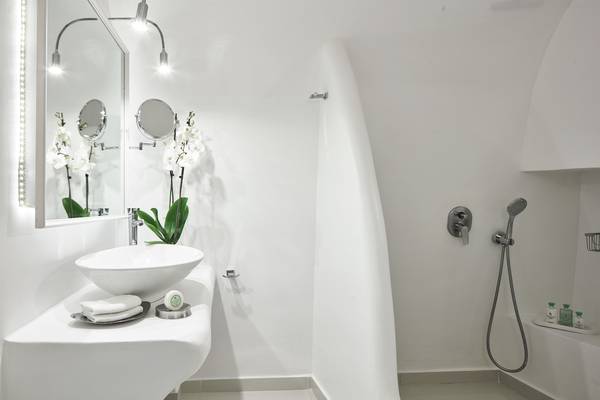 Badezimmer im Katikies Chromata Hotel auf Santorini mit einem weißen Waschbecken, Spiegel und Dusche.