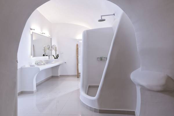 Badezimmer im Katikies Chromata Santorini Hotel mit weißer Architektur, Waschbecken und Dusche.