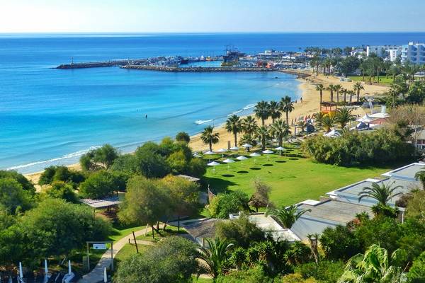 Luftaufnahme des Grecian Bay Hotels, Strand und Meer mit vielen Palmen und weißen Sonnenschirmen.