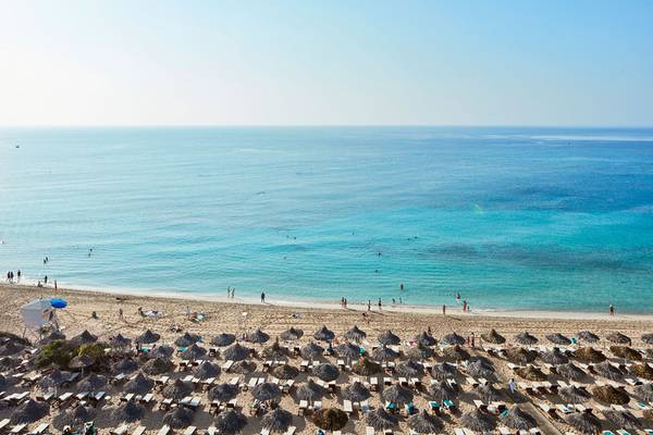 Luftaufnahme des Grecian Bay Hotels mit Strand, Liegestühlen und Sonnenschirmen.