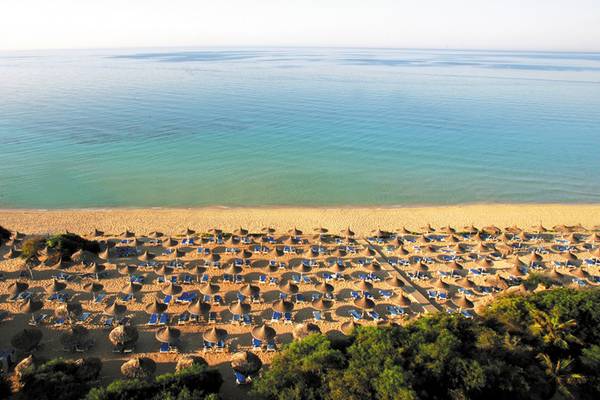 Luftaufnahme des Strandes des Grecian Bay Hotels mit vielen Sonnenliegen und Sonnenschirmen.