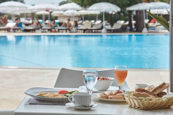 Frühstück am Pool im Grecian Bay Hotel mit Blick auf das Schwimmbecken und Sonnenschirmen.