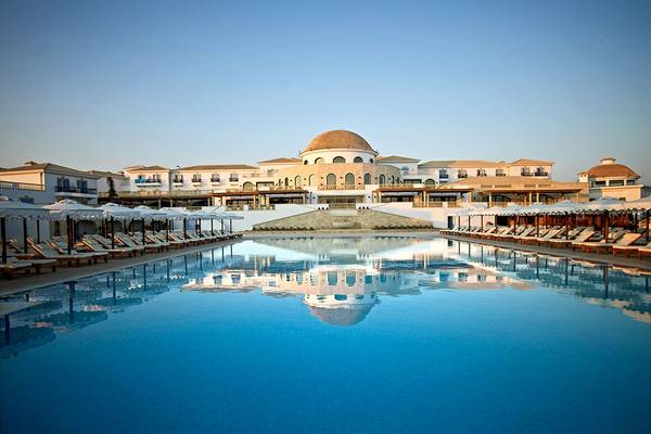 Außenpool mit Sonnenliegen und einem großen Hotelgebäude im Hintergrund.