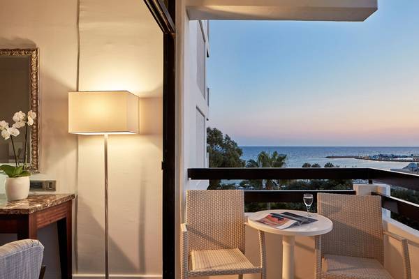 Balkon mit Meerblick im Grecian Bay Hotel mit einem Tisch, zwei Stühlen und einem Lampen.