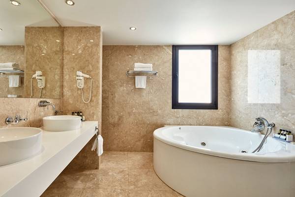 Badezimmer im Grecian Bay Hotel mit Marmorwänden, zwei Waschbecken und Badewanne.