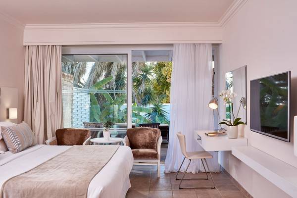 Innenansicht eines Zimmers im Grecian Bay Hotel mit Bett, Stühlen und Fernseher.