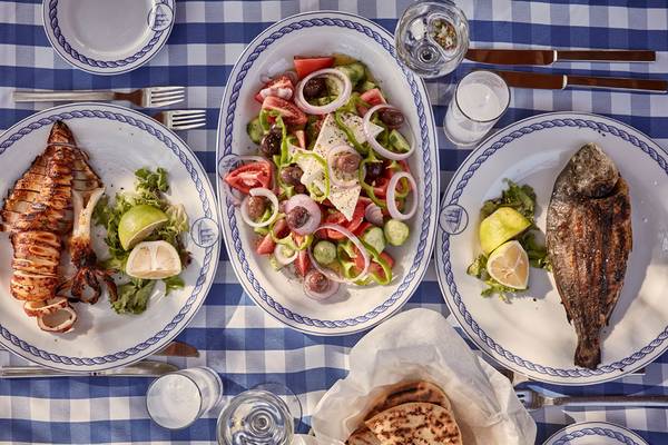 Griechisches Essen auf blauem Karotisch, inklusive gegrillter Tintenfisch, Salat und gebackener Fisch.
