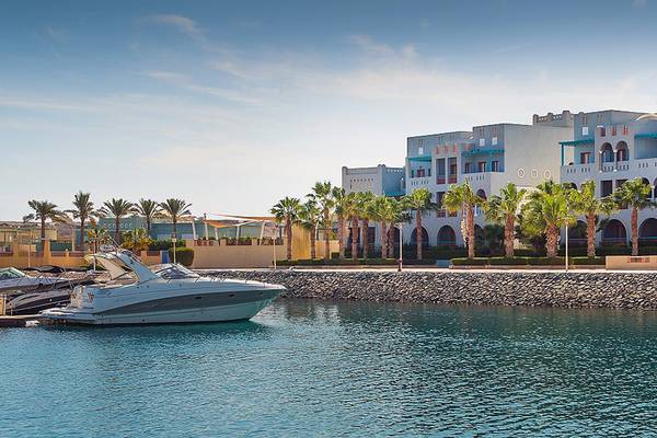 Außenansicht des Fanadir Hotel El Gouna mit weißen Gebäuden, blauen Fenstern und Palmen im Vordergrund.