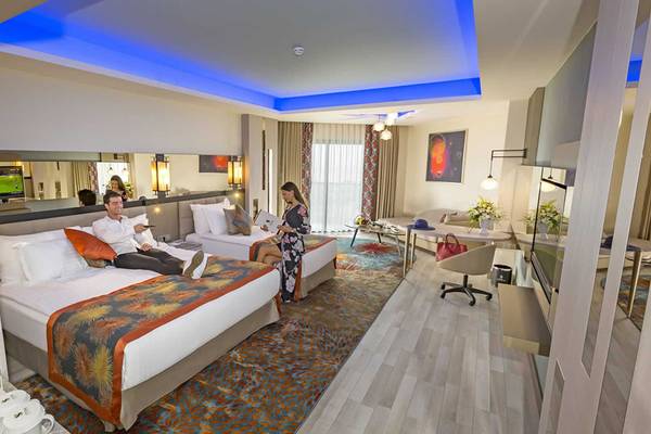 Zwei Betten in einem eleganten Hotelzimmer von Royal Seginus mit einer Frau, die liest, und einem Mann, der entspannt.