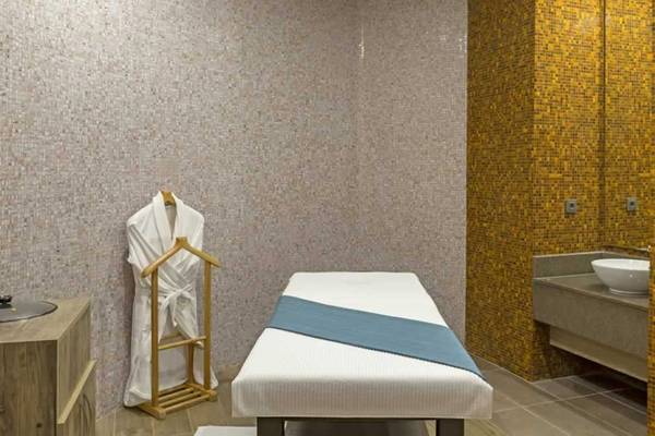 Massageraum im Royal Seginus Hotel mit einem Behandlungstisch, einem Bademantel und einem Waschbecken.