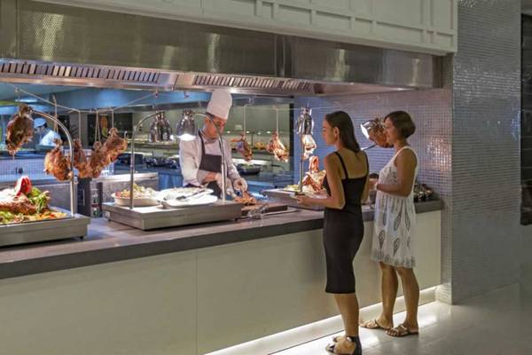Gastronomiebereich des Royal Seginus Hotels mit einem Koch und Gästen an der Fleischtheke.