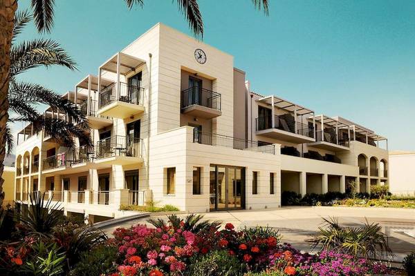 Außenansicht des Aegean Pearl Hotels mit Uhr und Blumengarten vor der Fassade