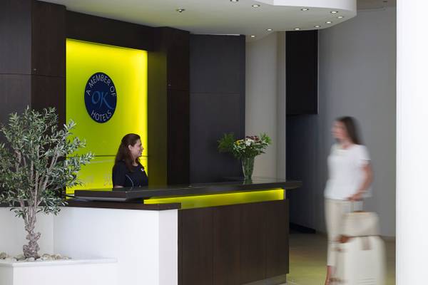 Empfang des Kriti Beach Hotels mit Rezeptionistin und Gast, die mit Gepäck unterwegs ist.