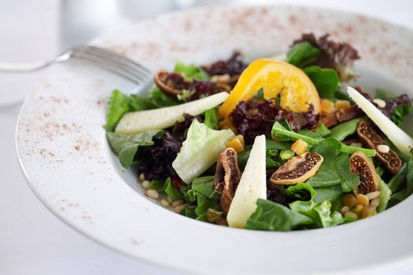 Salat in einem weißen Teller mit Obst und Nüssen.