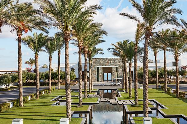 Eingangsbereich des Amirandes Grecotel Boutique Resorts mit hohen Palmen und einem Wasserbecken.