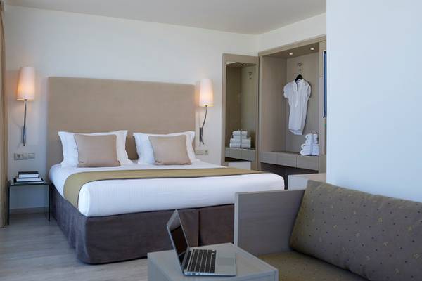 Schlafzimmer im Kriti Beach Hotel mit Doppelbett, Nachttischen und Laptop auf Beistelltisch.