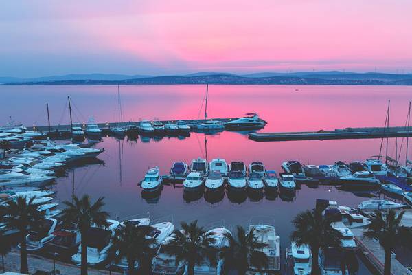 Ein Hafen mit vielen weißen Booten, die bei einem pinkfarbenen Sonnenuntergang verankert sind.