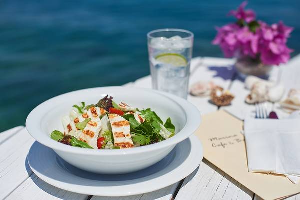 Ein weißer Teller mit Salat und Tomaten steht auf einem Tisch mit Meerblick.