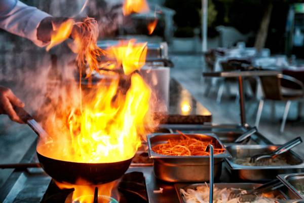 Ein Koch kocht mit Feuer in einer Pfanne auf einer Gasherd im Restaurant.