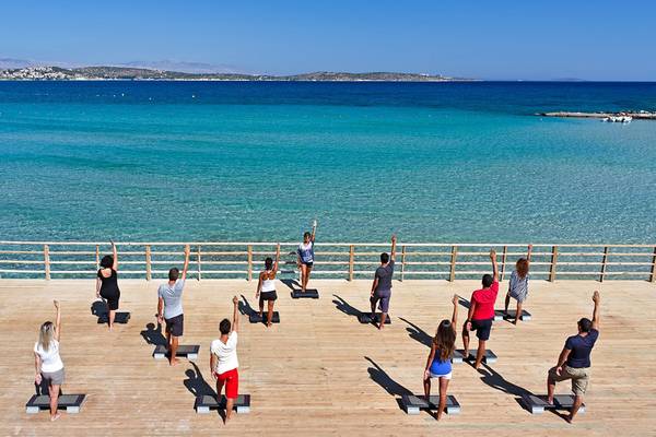 Yoga-Kurs auf Holzplattform am Meer mit Blick auf kristallklares Wasser.