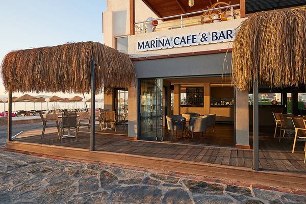 Außenansicht des Marina Cafe & Bar des Altin Yunus Hotels mit Strohdächern und Tischen im Freien.