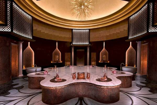 Innenansicht des Spas im Anantara Eastern Mangroves Abu Dhabi Hotel mit Marmortisch, Badewannen und Kronleuchter.