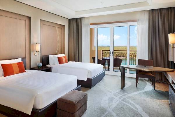 Suite-Zimmer im Anantara Eastern Mangroves Abu Dhabi Hotel mit zwei Betten, Schreibtisch und Balkon.