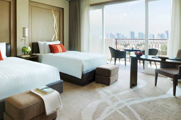 Suite-Zimmer im Anantara Eastern Mangroves Abu Dhabi Hotel mit zwei Betten, Kissen, Tisch, Stühlen und Balkon mit Stadtblick.
