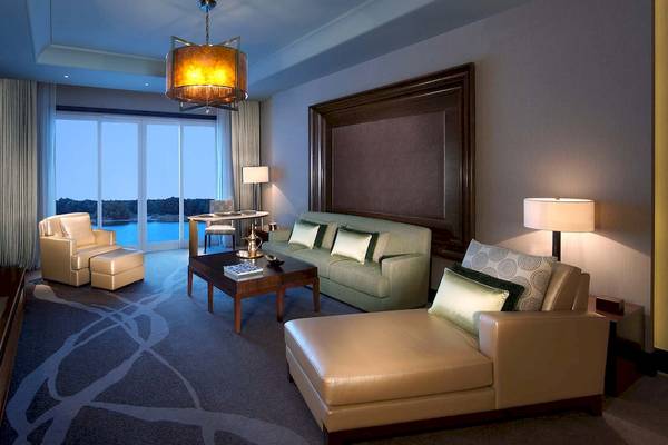 Wohnzimmer des Anantara Eastern Mangroves Abu Dhabi Hotels mit Sofa, Fernseher, Couchtisch, Lampe und Aussicht auf einen See.