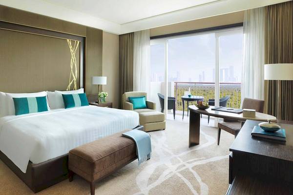 Schlafzimmer im Anantara Eastern Mangroves Abu Dhabi Hotel mit großem Bett, Kissen, Nachttischen, Lampe, Sessel, Schreibtisch und Stadtblick.