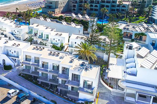 Luftaufnahme des Adele Beach Hotels am Strand mit mehreren Gebäuden und Sonnenliegen.