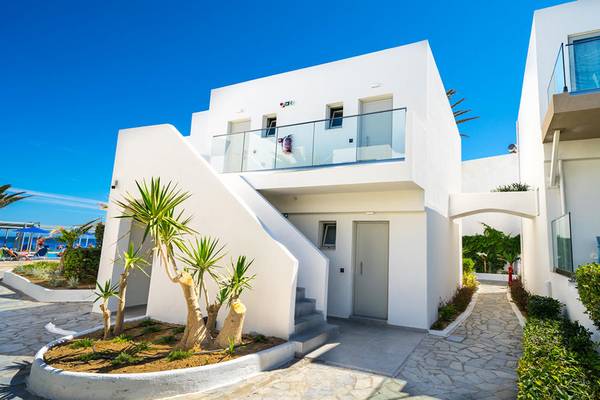 Die Vorderansicht des Adele Beach Hotels zeigt eine weiße Architektur mit Glasbalkonen und einer gepflasterten Einfahrt.