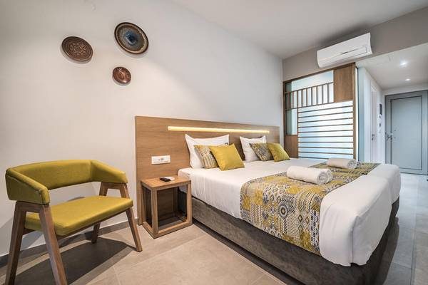 Ein elegantes Hotelzimmer im Adele Beach Hotel mit einem Bett, gelben Kissen und einem grünen Stuhl.