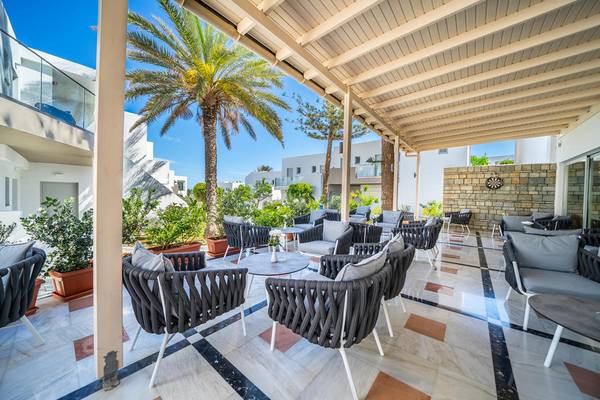 Terrasse des Adele Beach Hotels mit Lounge-Sesseln und Pflanzen, beschattet von einer Pergola.