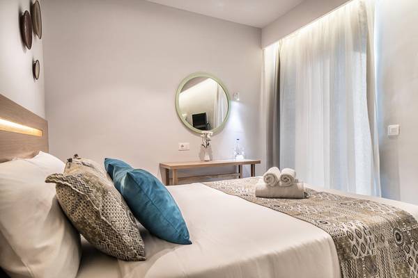 Schlafzimmer im Adele Beach Hotel mit einem Bett, Kissen, Spiegel und Nachttisch.