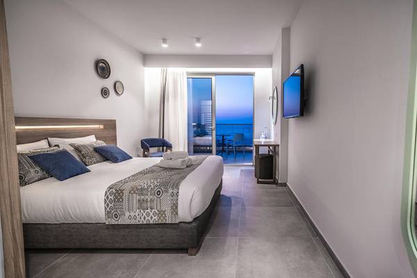 Innenansicht eines Hotelzimmers im Adele Beach Hotel mit einem Doppelbett, einem Fernseher und einem Balkon.