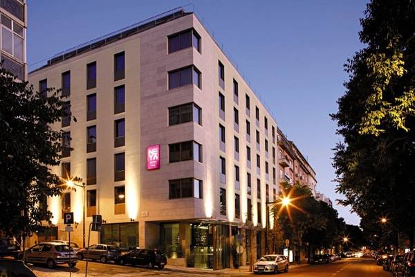 Abendansicht des Neya Lisboa Hotels mit beleuchteten Fenstern und geparkten Autos.