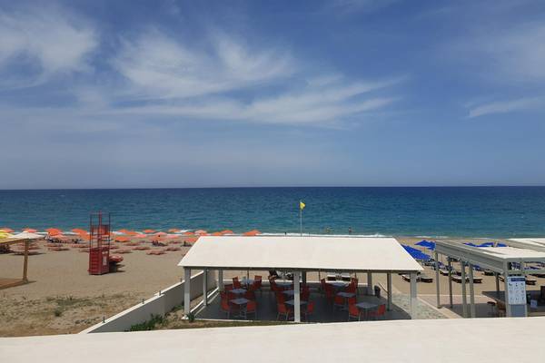Aussicht vom Adele Beach Hotel auf den Strand mit Sonnenschirmen und Tischen.