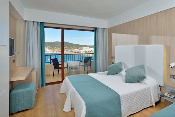 Zimmer im NYX Ibiza Hotel mit Balkon und Meerblick, ausgestattet mit zwei Betten, Sesseln und einem Schreibtisch.