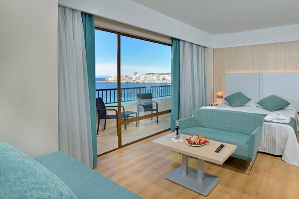 Zimmer im NYX Ibiza Hotel mit Balkon und Meerblick, inklusive Bett, Couch, Tisch und Stühle.