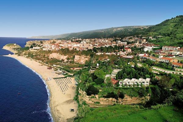 Luftaufnahme des Aldiana Club Rocca Nettuno Calabria mit Strand, Klippe und grünen Hügeln.
